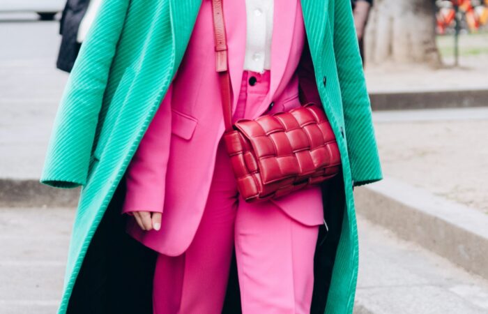 Person wearing a vibrant pink suit paired with a green textured overcoat and carrying a signature woven red Bottega Veneta bag, photographed on a city street.