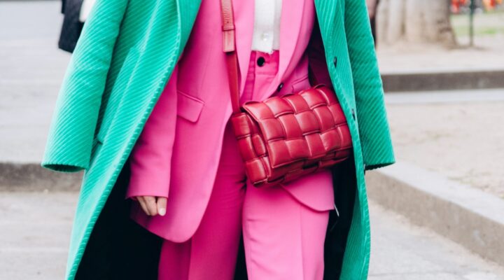 Person wearing a vibrant pink suit paired with a green textured overcoat and carrying a signature woven red Bottega Veneta bag, photographed on a city street.